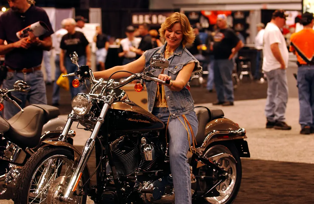 A visitor sits on a black and bronze Harley-Davidson Deuce at an indoor motorcycle display.