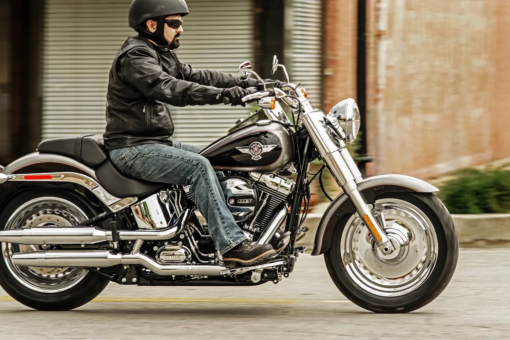 A rider on a black and silver 2016 Harley-Davidson Fat Boy FLSTF, seen from the right with its solid disc wheels and chrome exhaust.
