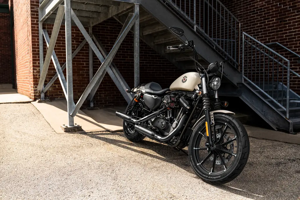 A Harley-Davidson Iron 883 with a cream tank and genuine accessories parked under an iron staircase