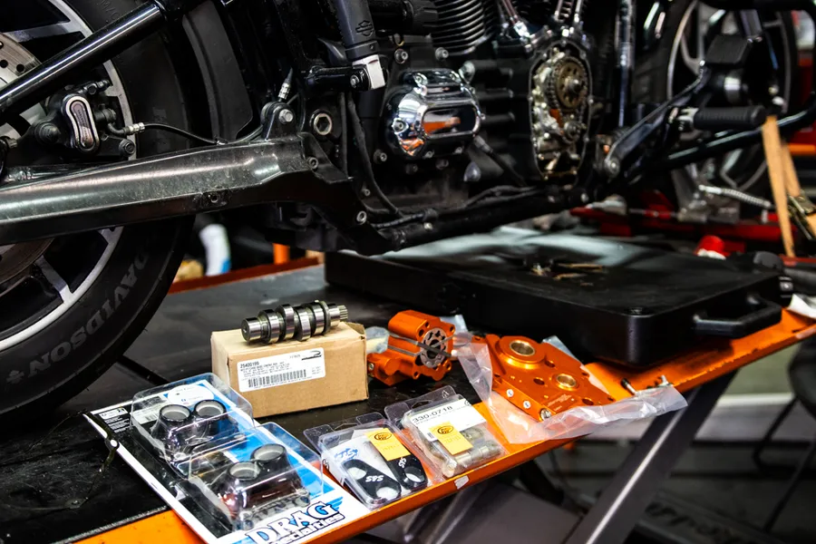 Drag Specialties parts laid out on workshop bench beside Harley-Davidson engine on lift
