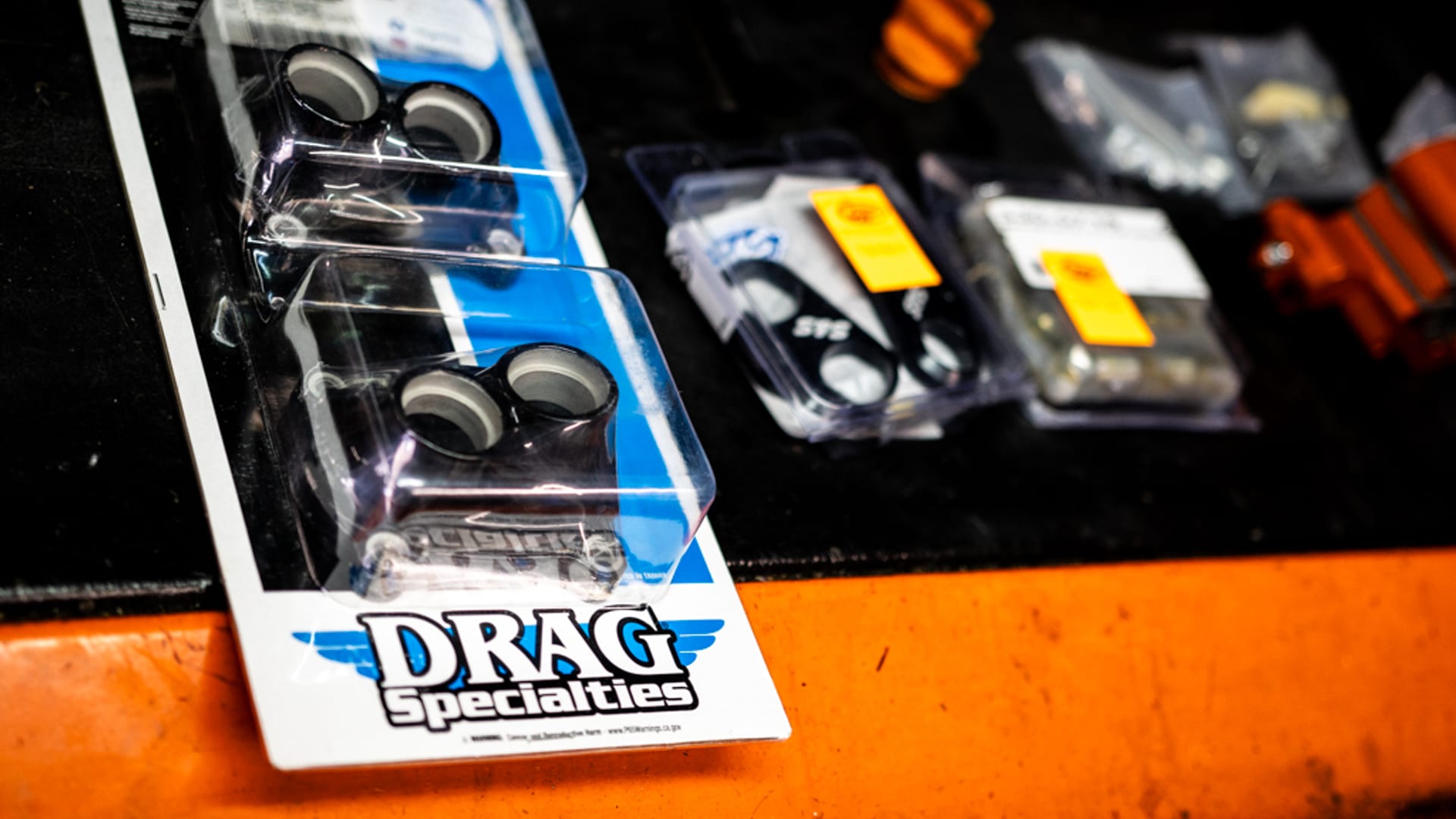 Drag Specialties blister-pack on dark workshop bench — iconic blue and white packaging