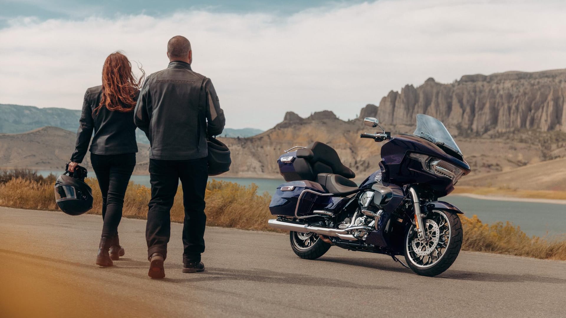 Two riders walking to a Harley-Davidson Road Glide touring motorcycle on the coast