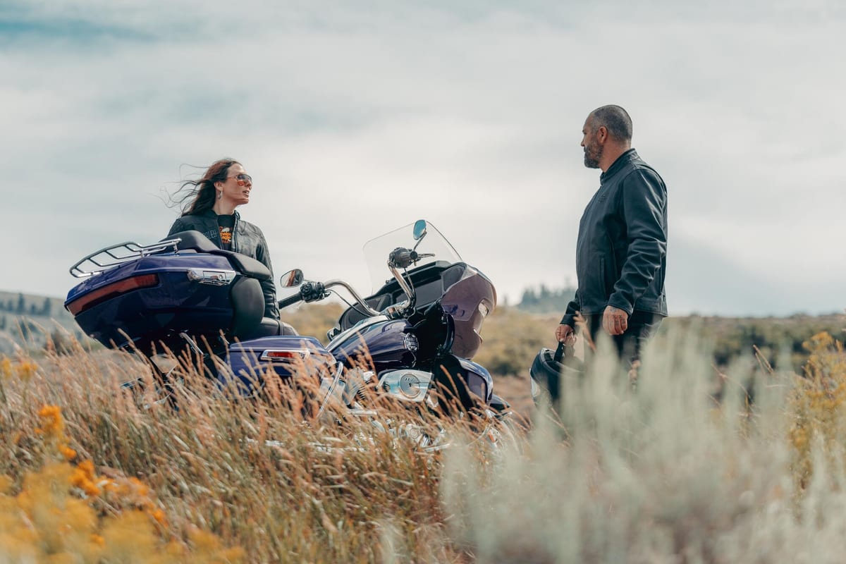 Two Harley-Davidson riders beside a Road Glide in open coastal country