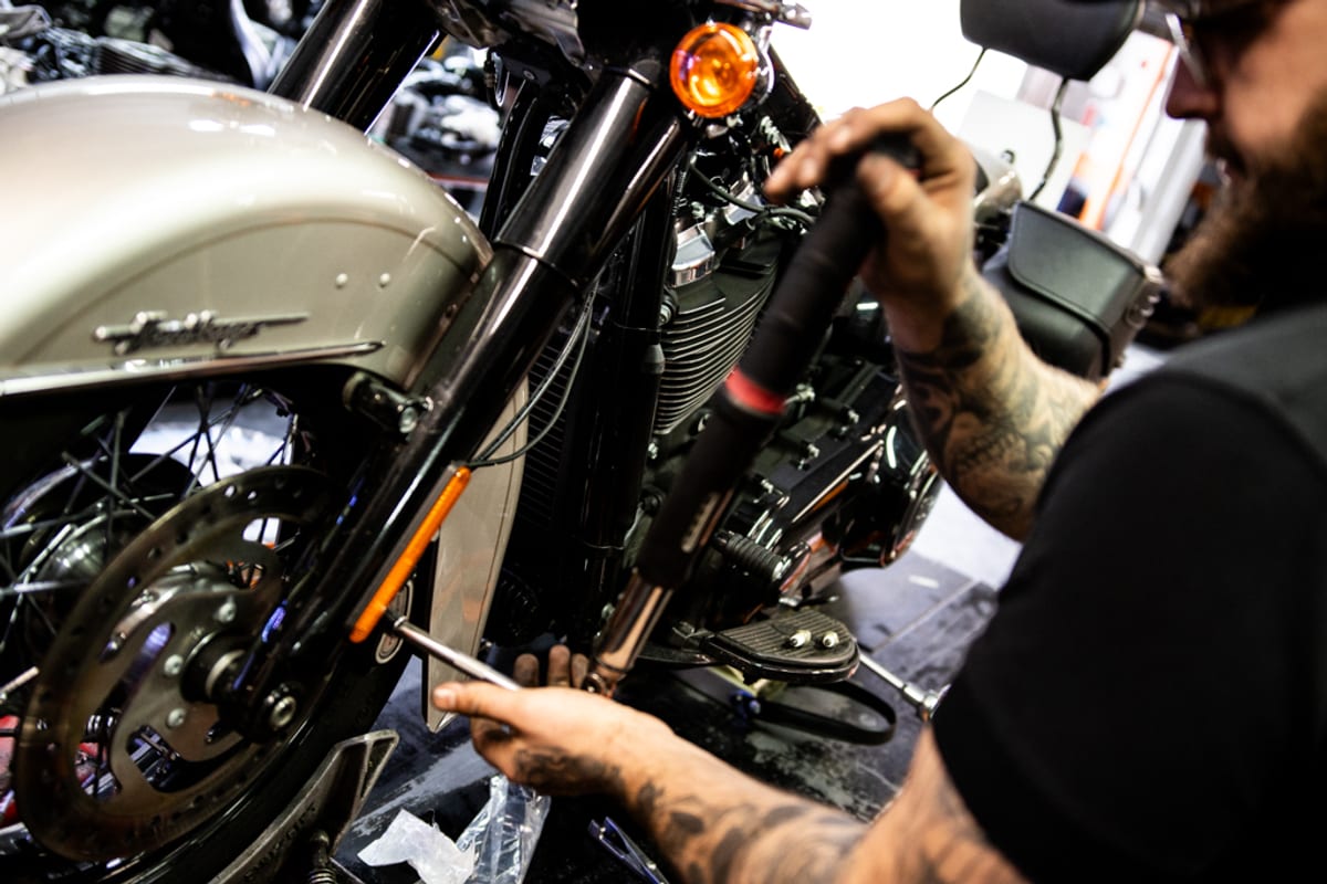 A mechanic working on the front wheel and forks of a Harley-Davidson during a service