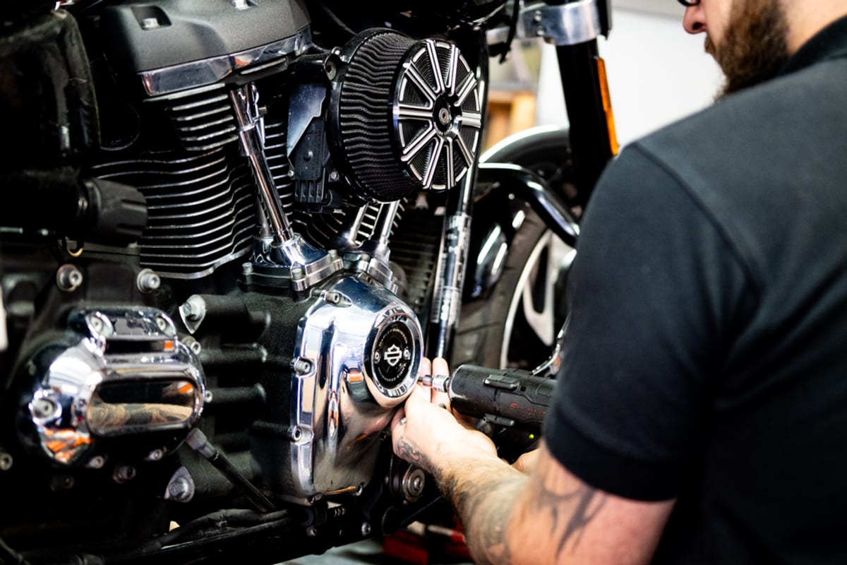 A technician using an impact wrench on a Harley-Davidson primary cover during a fluid change