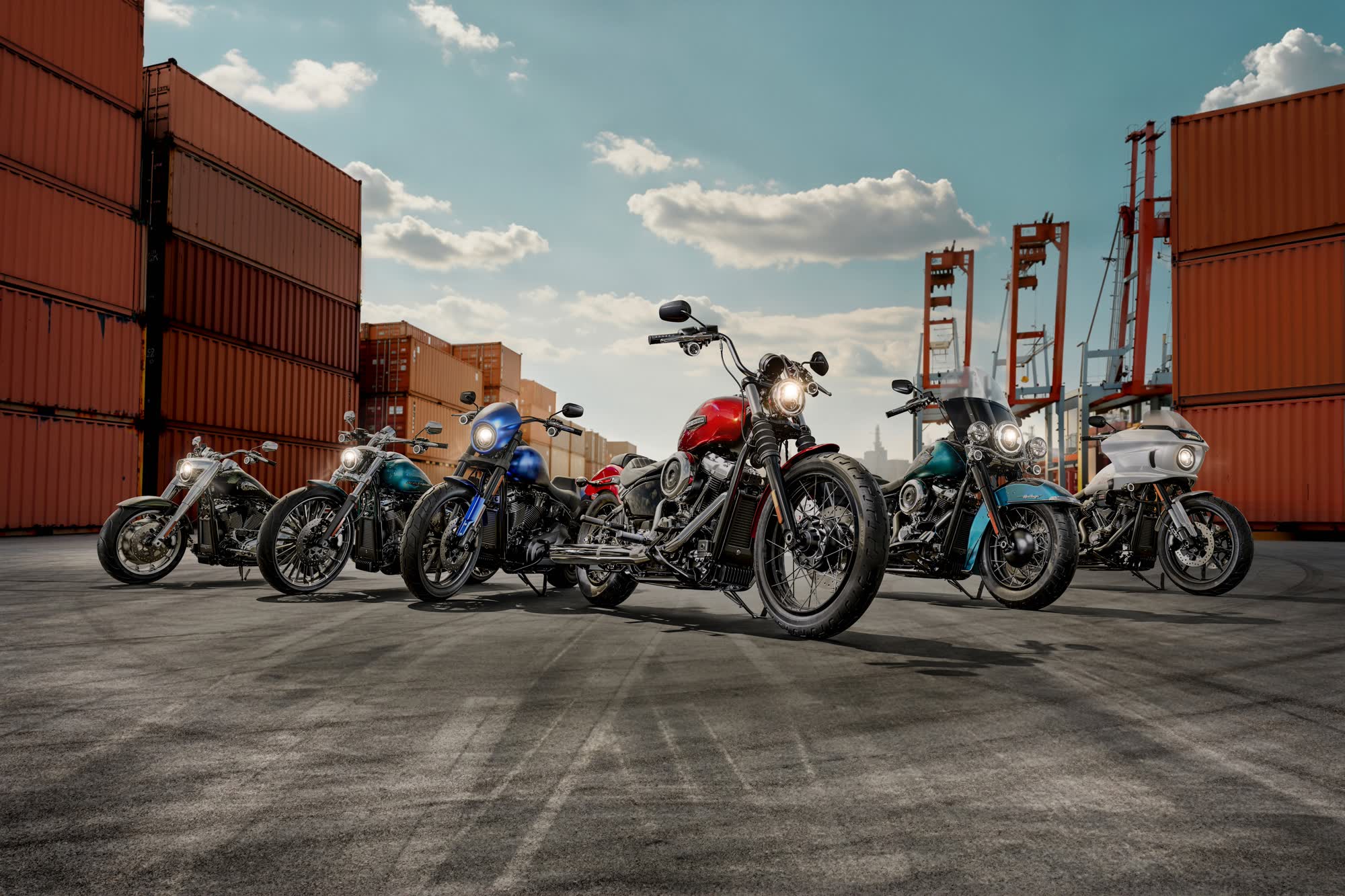 Six Harley-Davidson motorcycles lined up in a shipping container yard